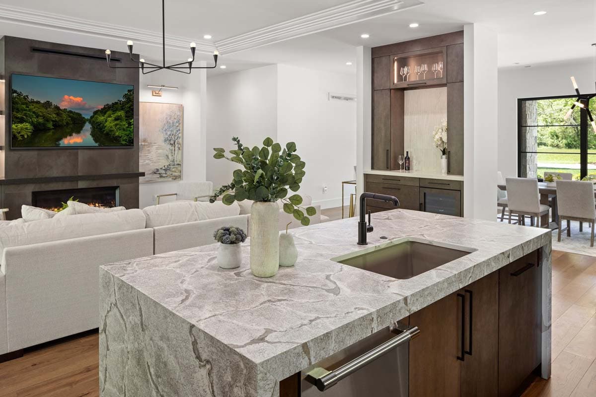 Open concept living area with fireplace, large TV, and kitchen island with sink. Built-in cabinetry and dining area visible.