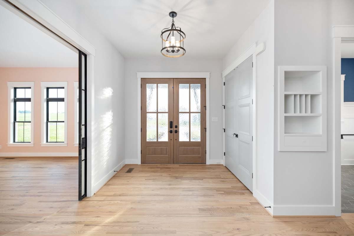Interior entry foyer with double glass doors, natural wood floors, a decorative light fixture, and a built-in wall shelf.