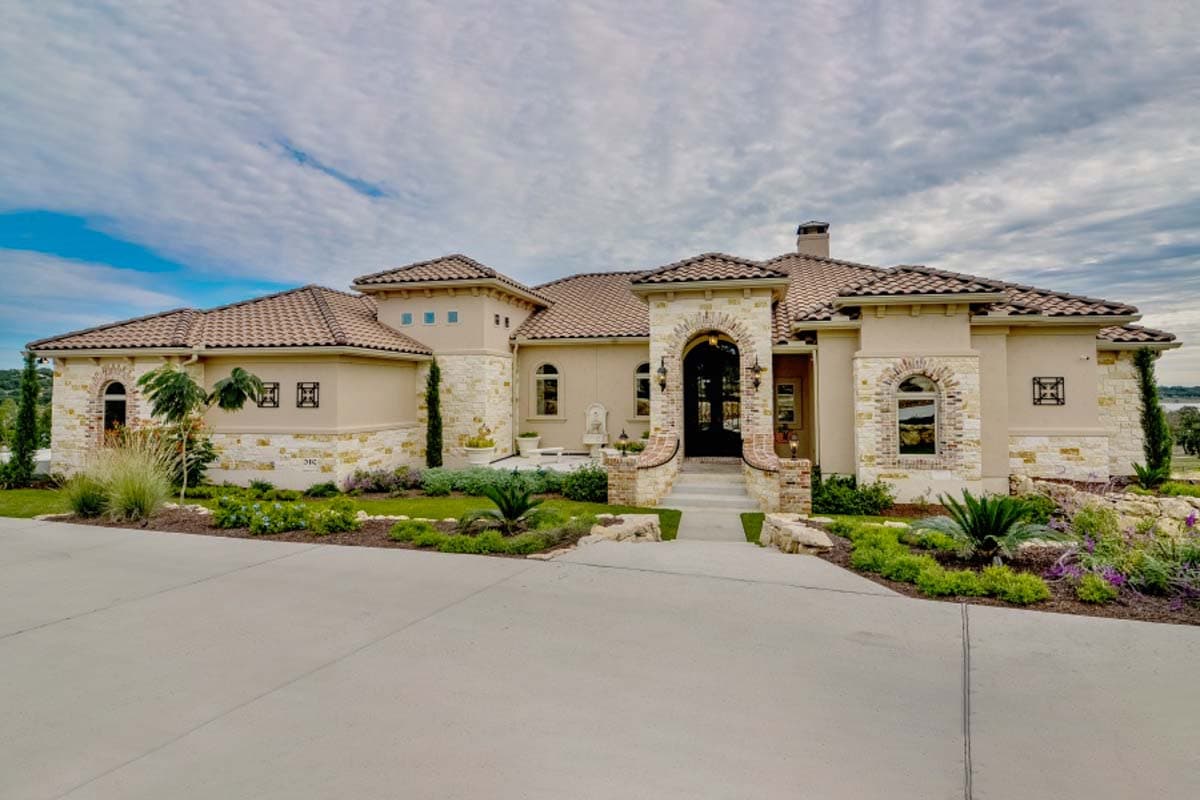 House plan exterior. One-story Mediterranean style. Features include barrel tile roof, arched entryway, stone veneer accents, and multiple dormers.