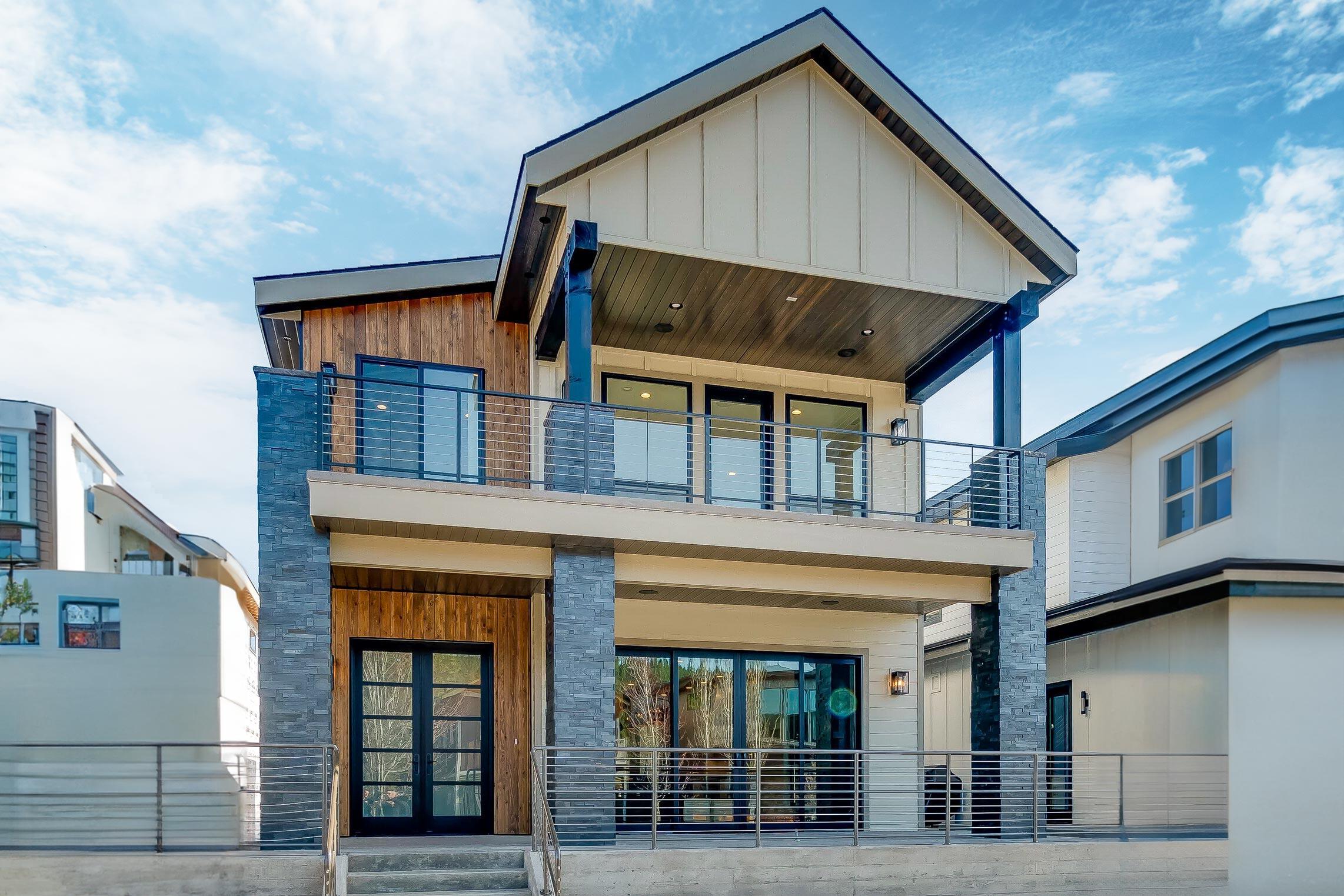 House plan exterior. Two-story modern home with wood and stone siding. Features include a gable roof, covered balcony, and floor-to-ceiling windows.