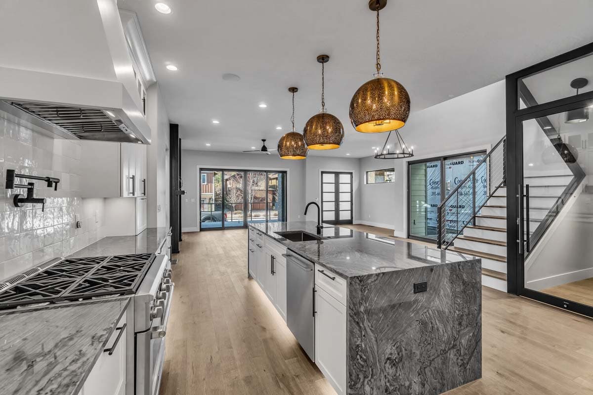 Open-concept kitchen and living area with island, modern staircase, and large sliding glass doors.