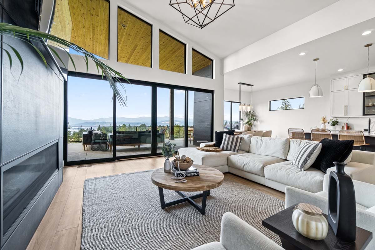 Open concept living room with a large sectional sofa, modern fireplace, and floor-to-ceiling windows showcasing a scenic view.