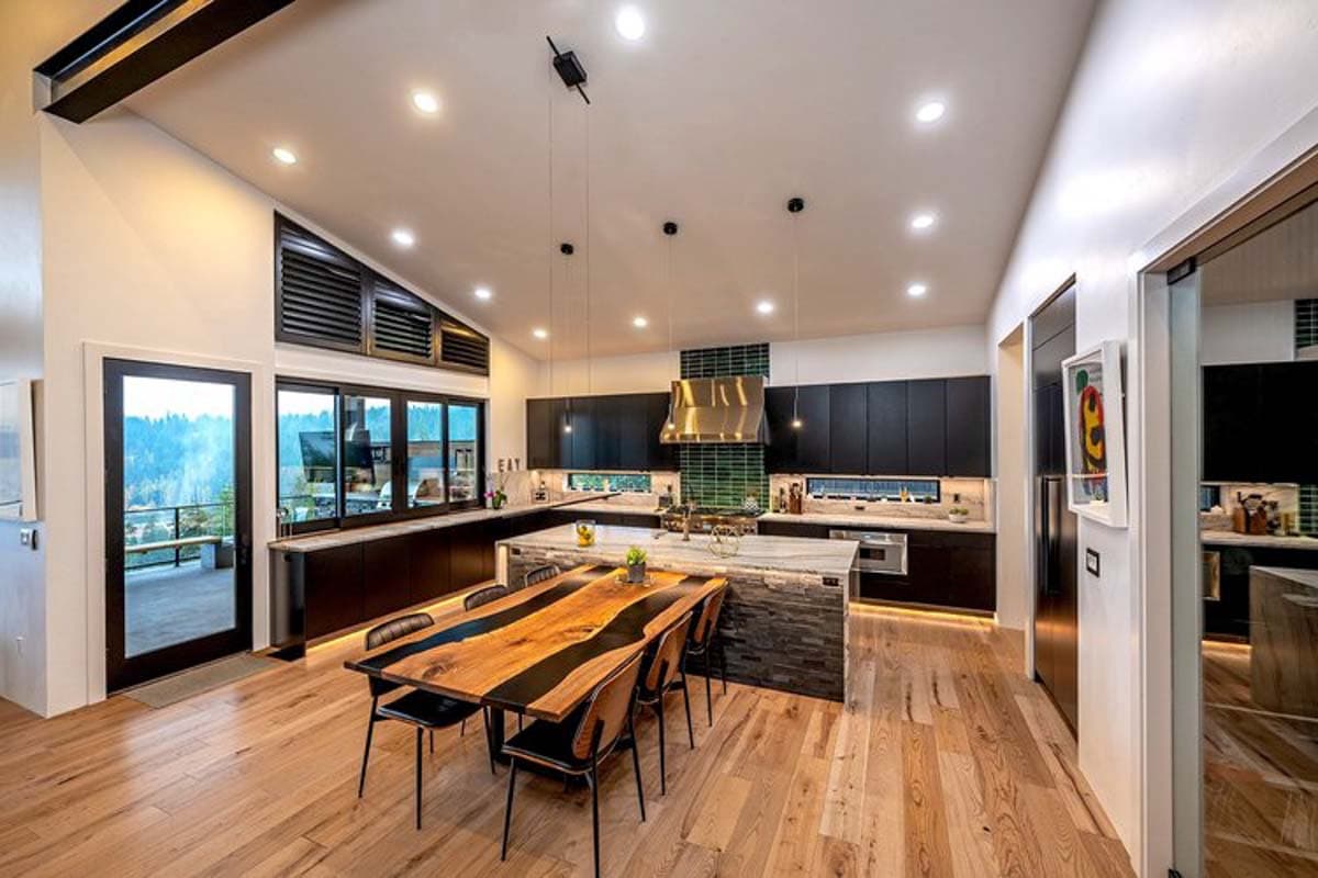 Open-plan kitchen with vaulted ceiling, island, dark cabinetry, large windows, and dining area.