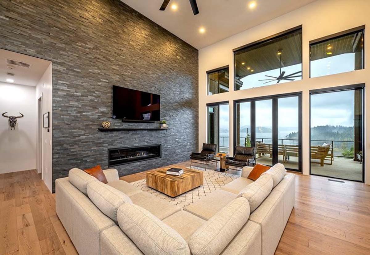 Living room with floor-to-ceiling stacked stone fireplace, large windows, sectional sofa, and wood floors.