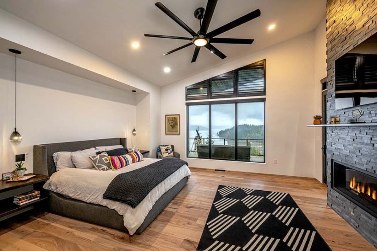 Primary bedroom with vaulted ceiling, large picture window, stone fireplace, and king-sized bed.