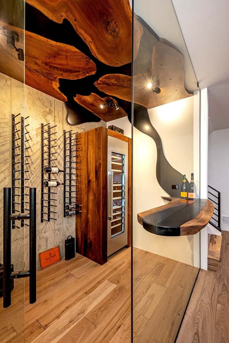 Wine cellar with wood slab ceiling, concrete walls, metal racks, wine fridge, and floating wood bar.