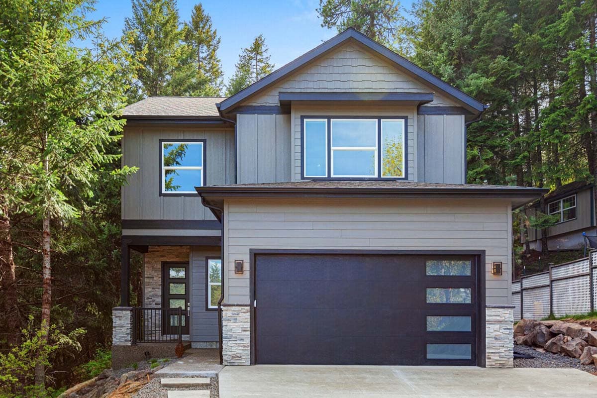 House plan exterior. Two-story modern house with a front-facing garage. Features include a gabled roof, stone accents, and large windows.
