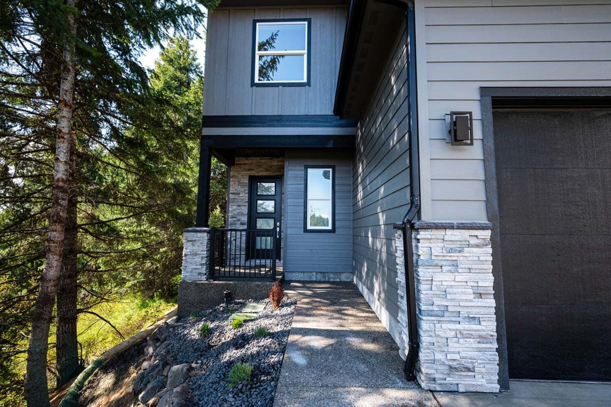 Two-story house plan exterior with a covered porch, modern siding, stone accents, and a two-car garage.