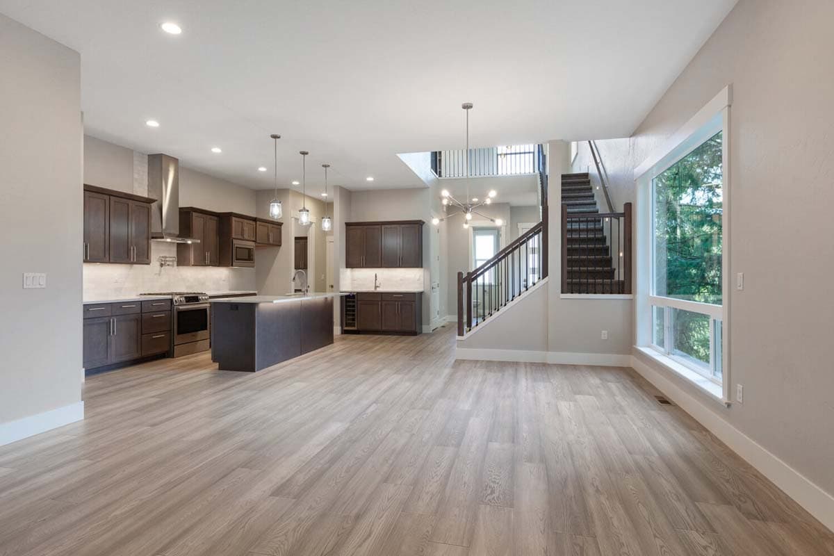 Open concept kitchen and great room with island, dark cabinetry, stainless steel appliances, and modern staircase with railing.