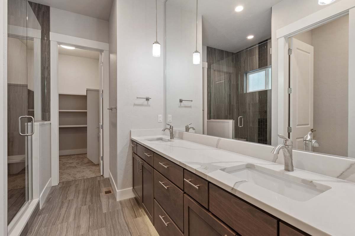 Bathroom with double vanity, modern pendant lights, glass-enclosed shower, and walk-in closet.