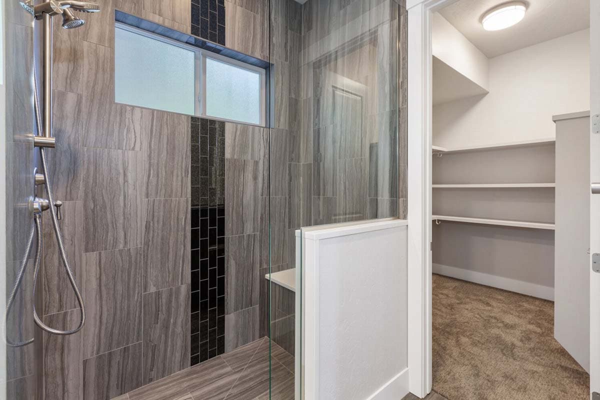 Modern bathroom with a walk-in shower featuring vertical gray wood-look tiles and a glass door, adjacent to a carpeted walk-in closet with shelves.