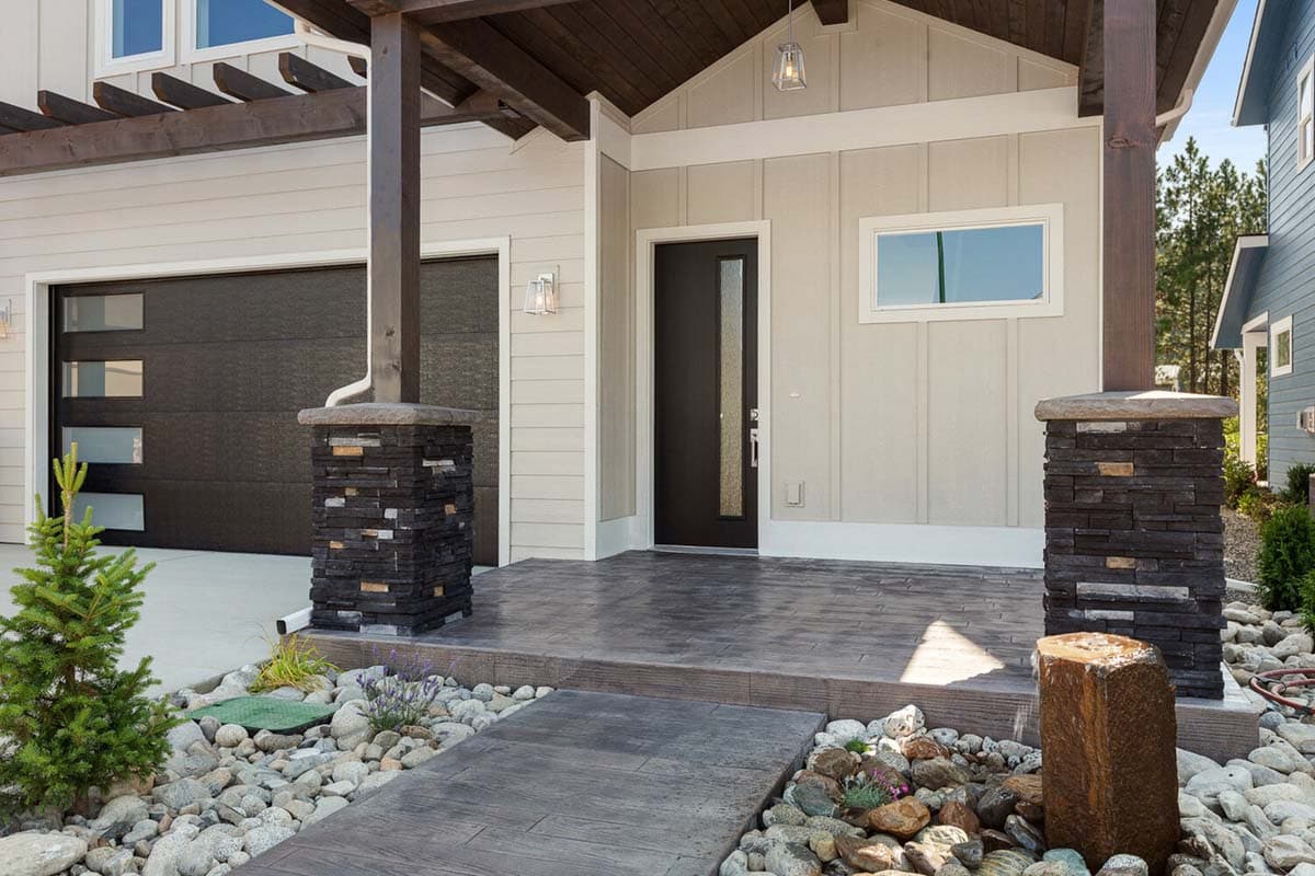 House plan exterior: Modern style with dark modern garage door, covered entry with stone pillars, and wood pergola.