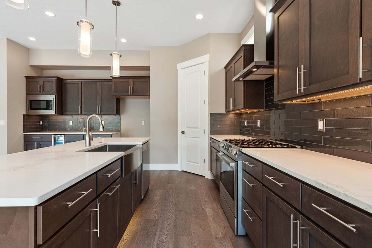 Kitchen with dark wood cabinets, white quartz island with sink, stainless steel appliances, and dark subway tile backsplash.