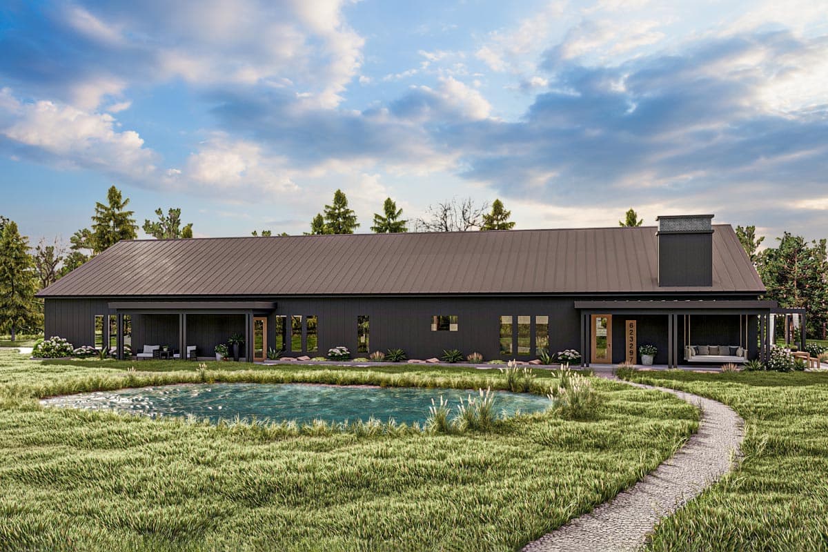 A modern, dark-colored house with a long, low profile. A pond sits in front, with a stone path leading towards the front porch with a porch swing.
