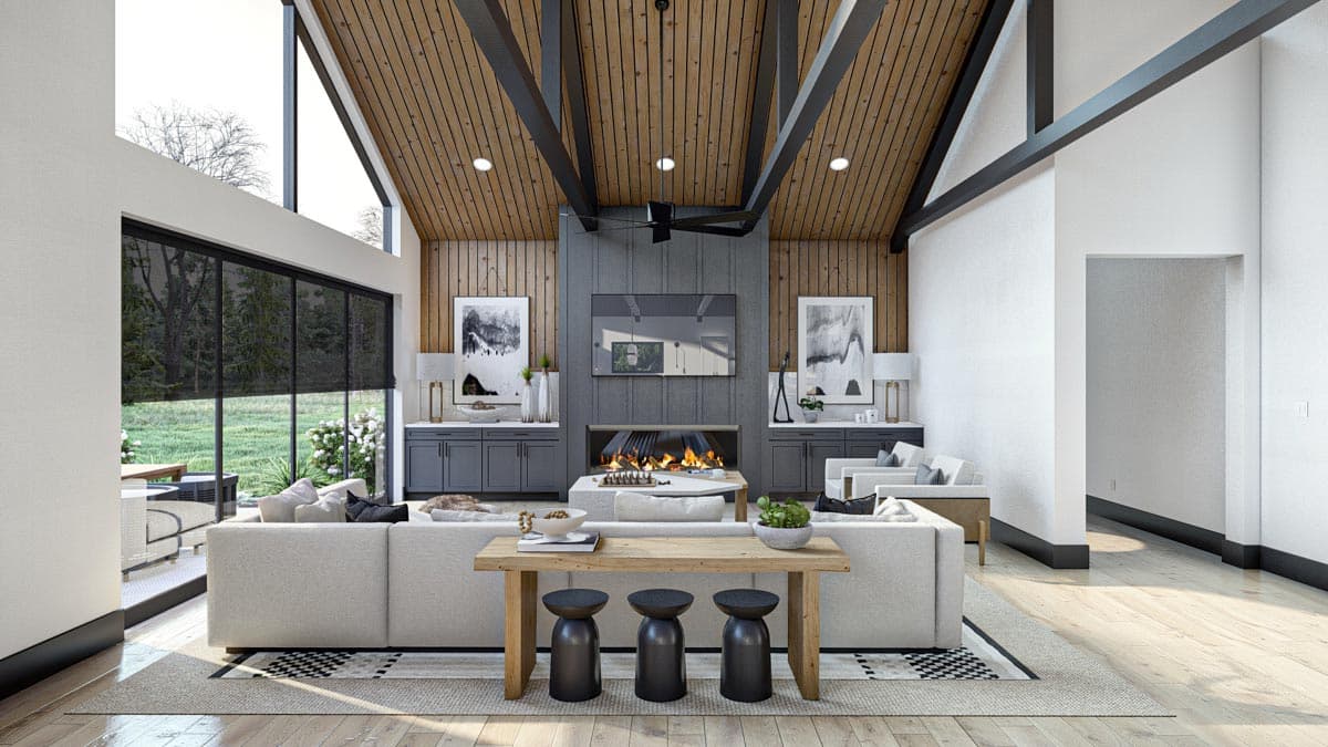 Modern living room with high vaulted wood ceiling and large windows. Features a fireplace, sofas, and a wooden table with stools.