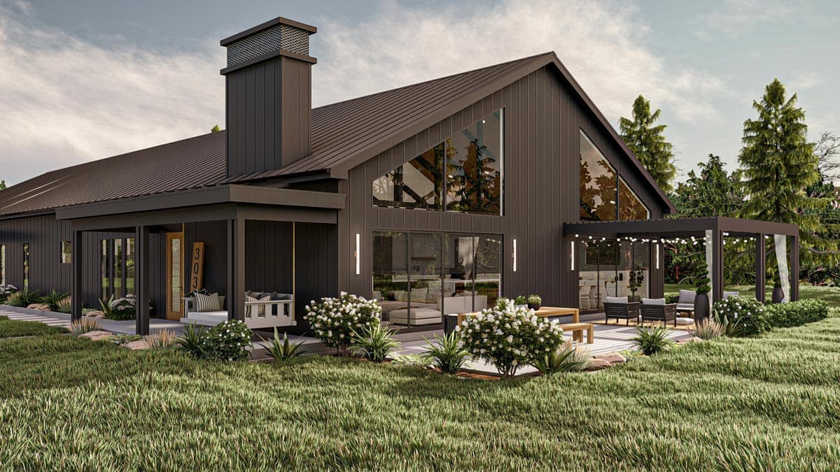 Modern, dark-colored house with a sloped roof, large windows, and outdoor seating area, blending into a green landscape.