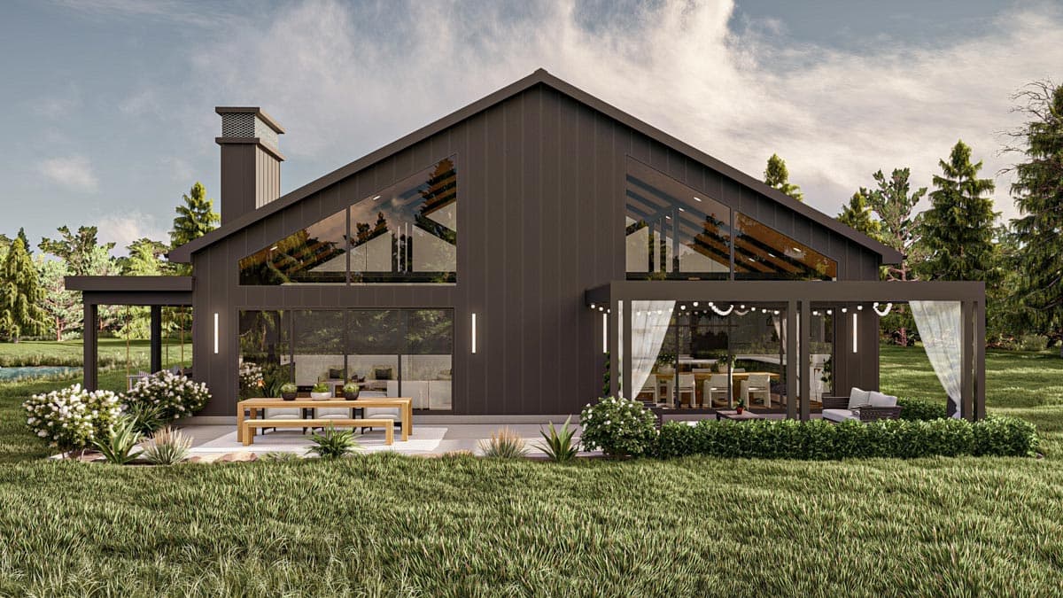 A modern, dark-colored house with large glass windows and an A-frame roof. An outdoor dining area and lush landscaping complete the design.