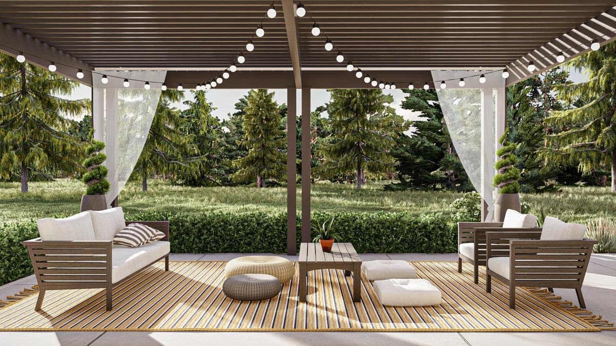 Outdoor patio with seating, rug, and coffee table beneath a wooden pergola strung with string lights. A green forest is visible in the background.