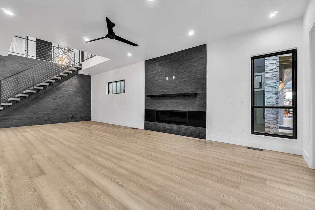 Modern living room with stone fireplace, open staircase with metal railing, and large window.
