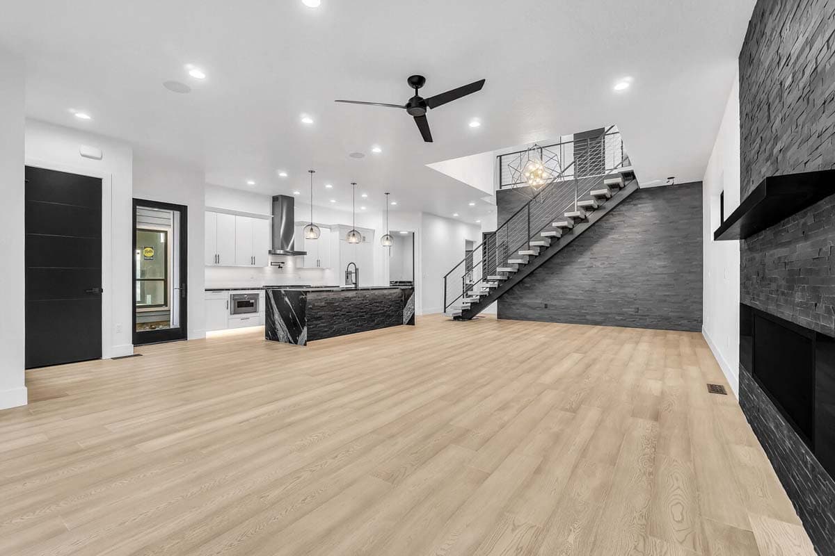 Open-concept living space with modern kitchen island, floating staircase with metal railing, and dark stone accent wall and fireplace.