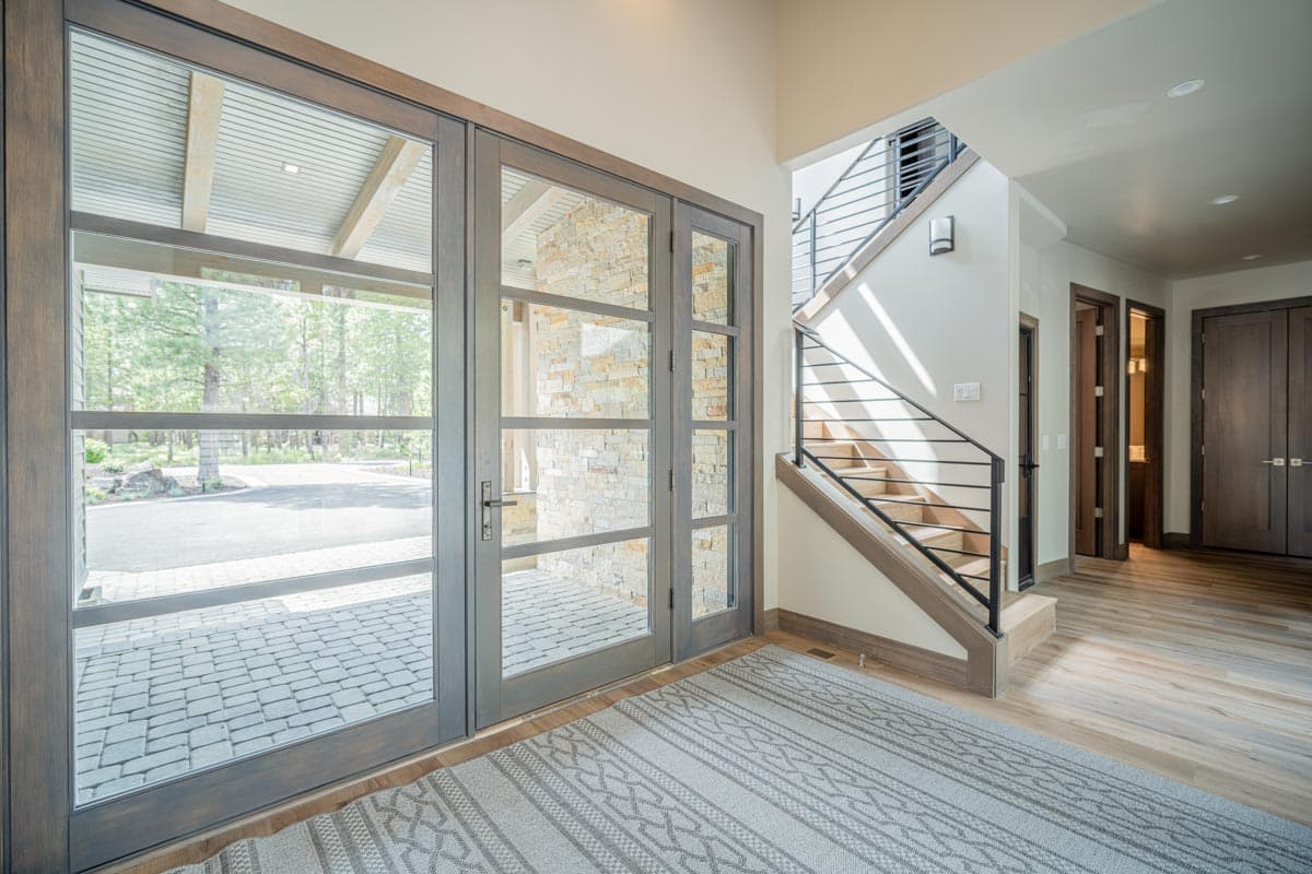 Entrance foyer with large glass doors, stone accent wall, and open-tread staircase with metal railing.