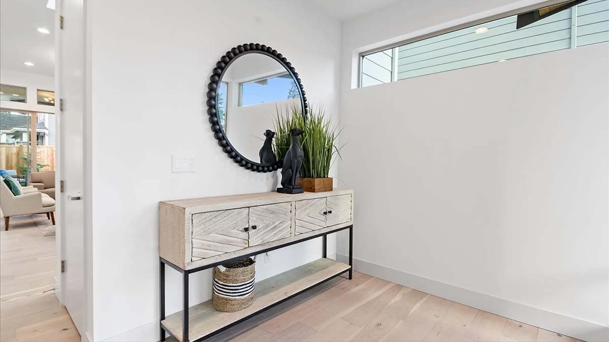 Interior view of entryway with console table, round mirror, decorative statues, and plant. Open doorway reveals living area.