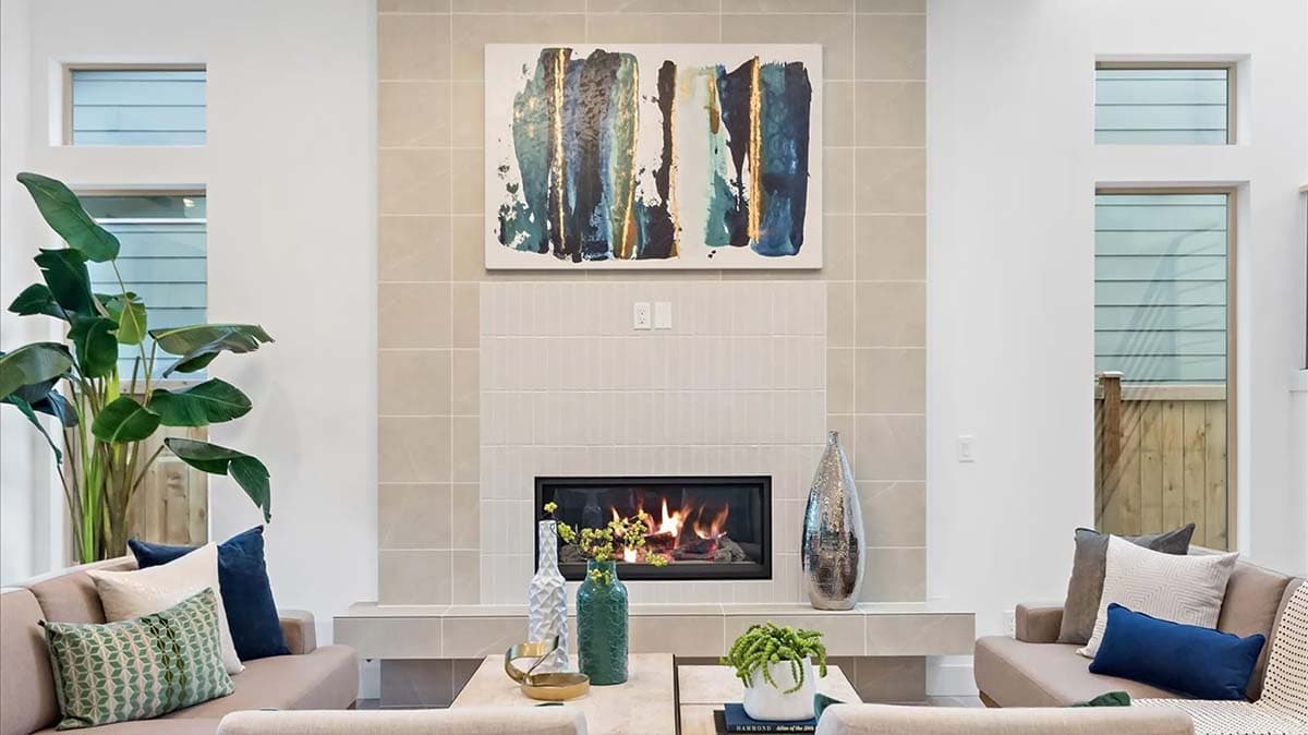 Interior view of a living room with a tiled fireplace, contemporary art, and a large plant.