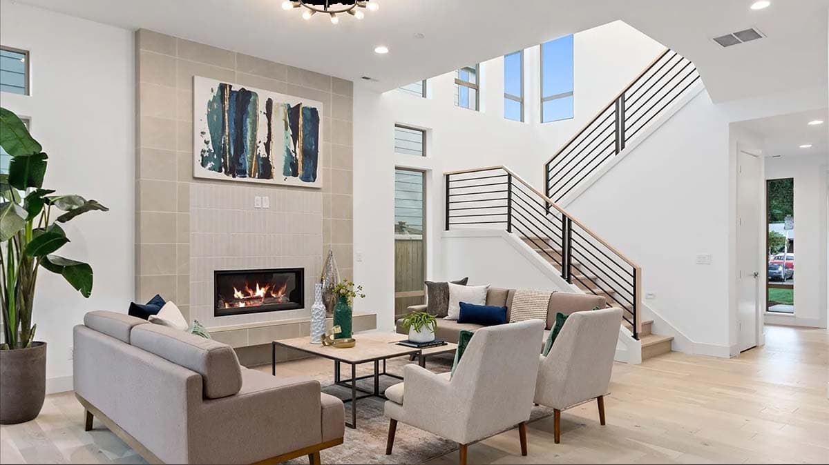 Interior view of a living room with a fireplace, seating area, and modern staircase with black railings.