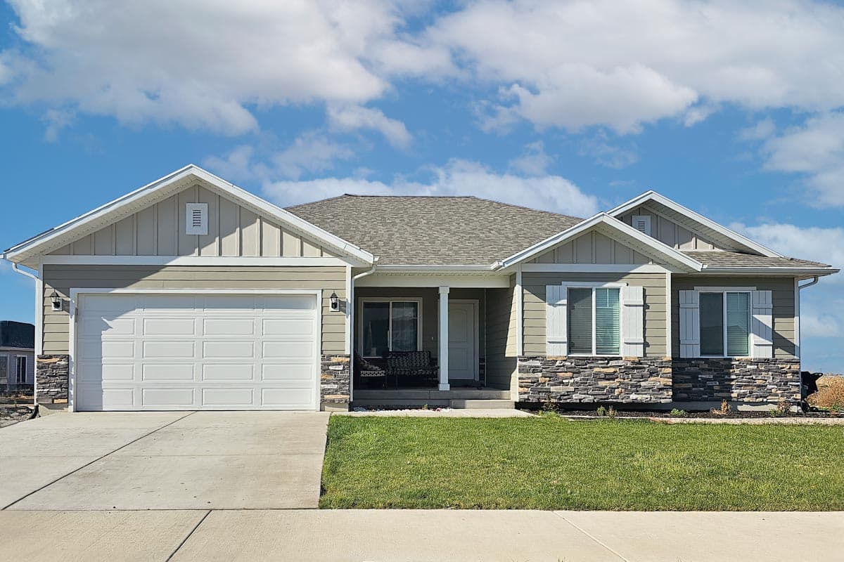 House plan exterior with two stories. Features include a front-facing garage, a covered porch, and gabled rooflines with decorative trim details.