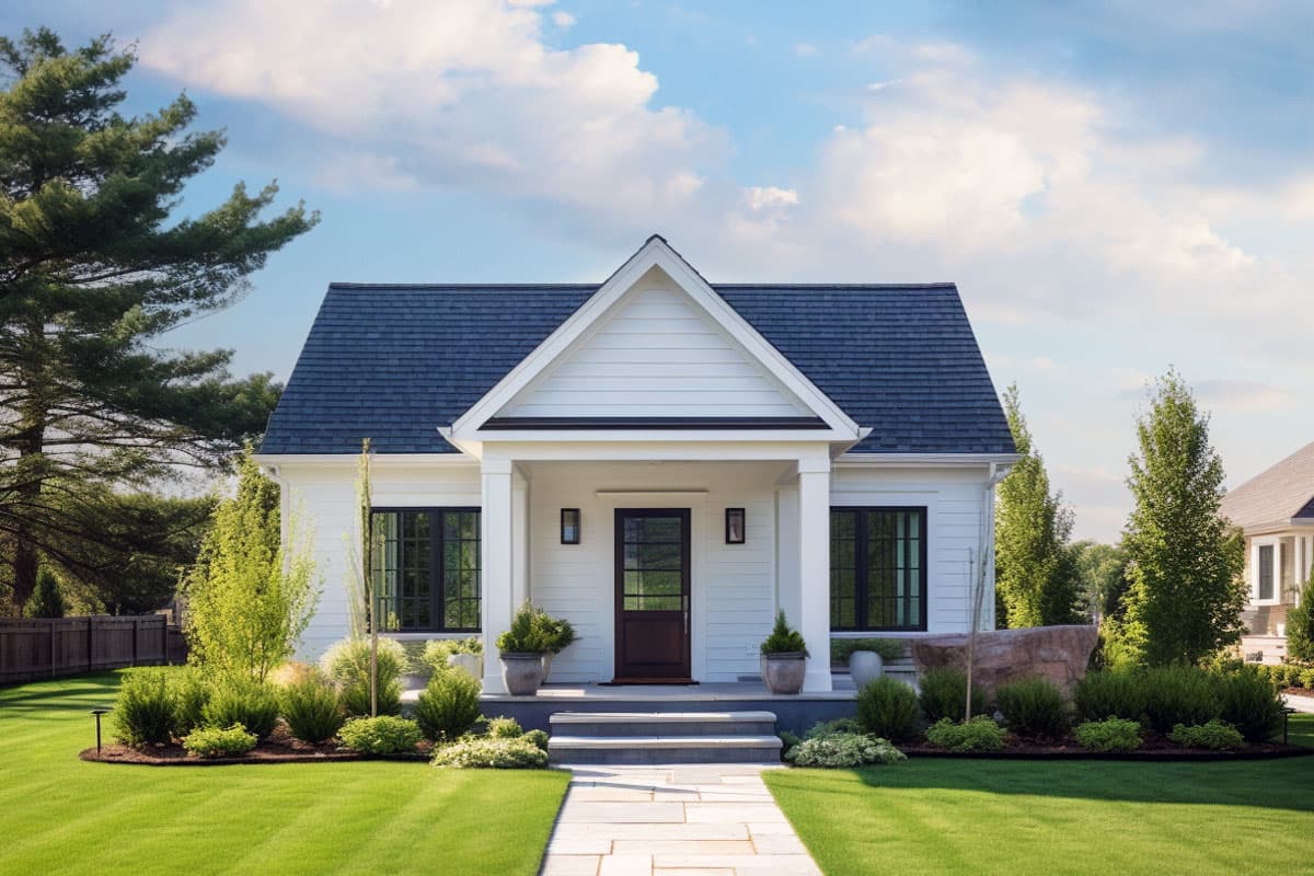 House plan exterior. White siding, gabled roof, and covered entry porch with columns. Features include dark-framed windows and a dark front door.
