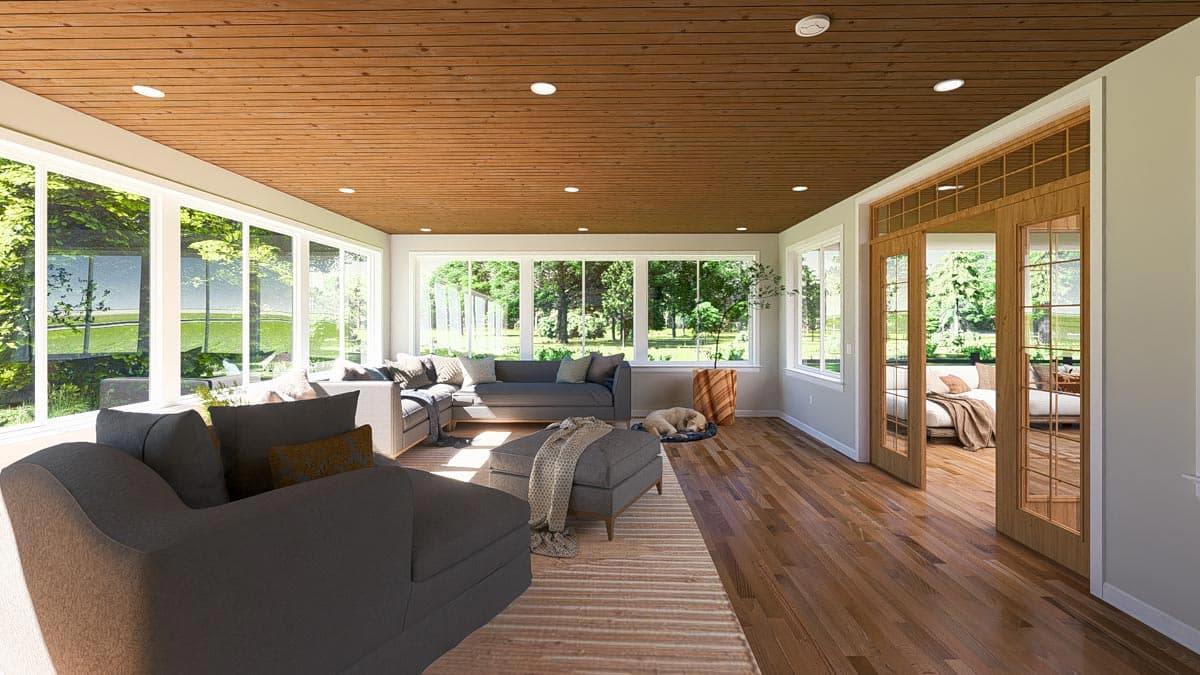 Sunroom interior with wood-paneled ceiling, sectional sofa, ottoman, and glass doors opening to outdoor seating area.