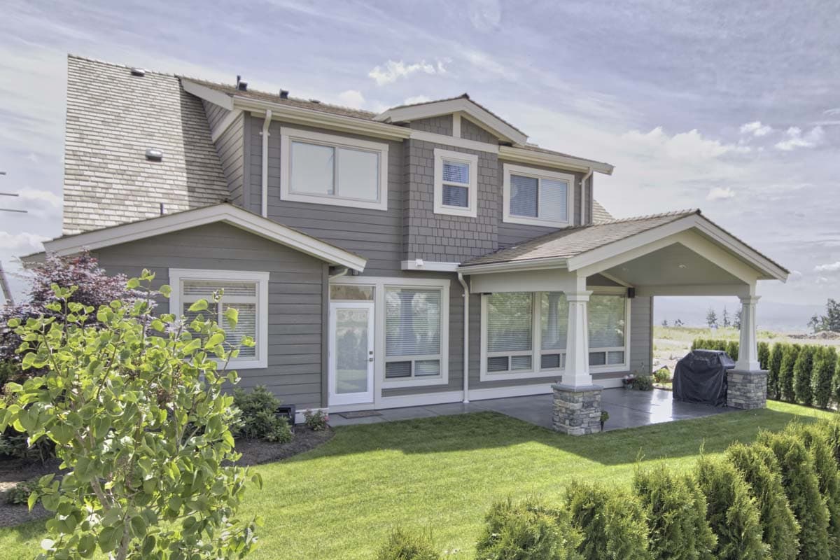 House plan exterior: Two-story home with shingle siding, gables, dormers, covered patio, and stone column accents.
