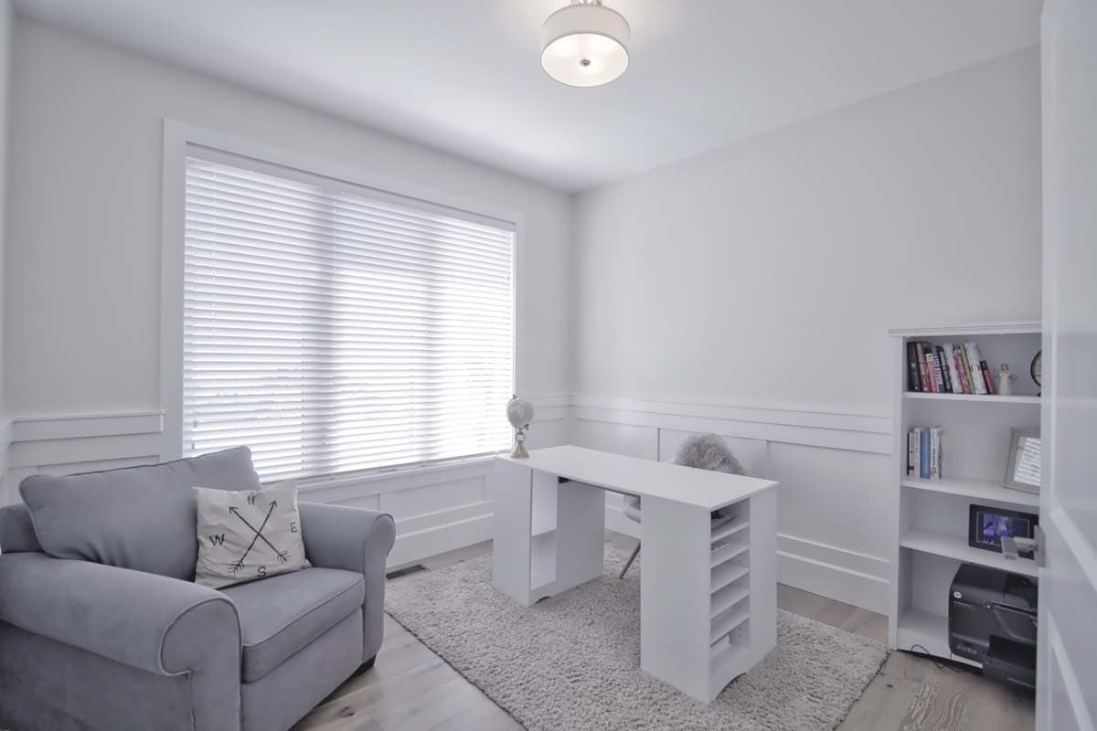Home office with gray armchair, white desk with globe, and bookshelf. Wide window with blinds.