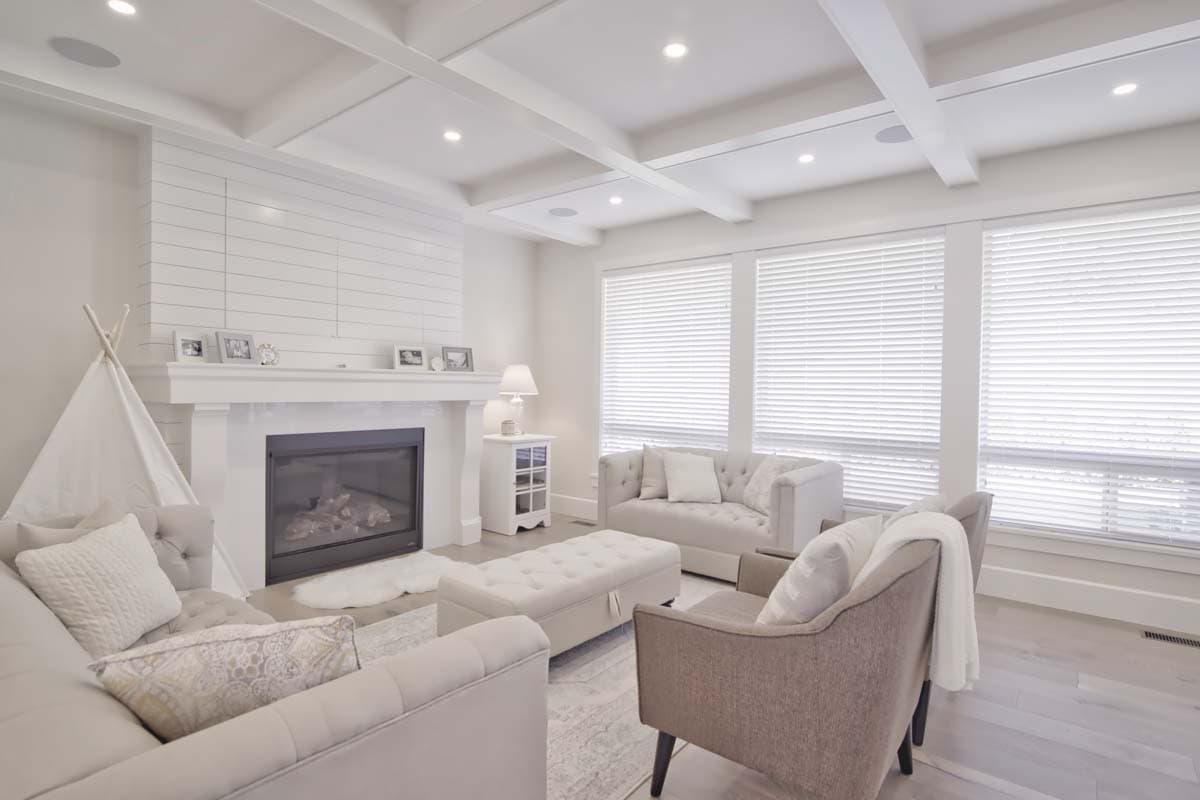 Living room with coffered ceiling, fireplace with shiplap surround, and large windows. Seating includes sofas and chairs.