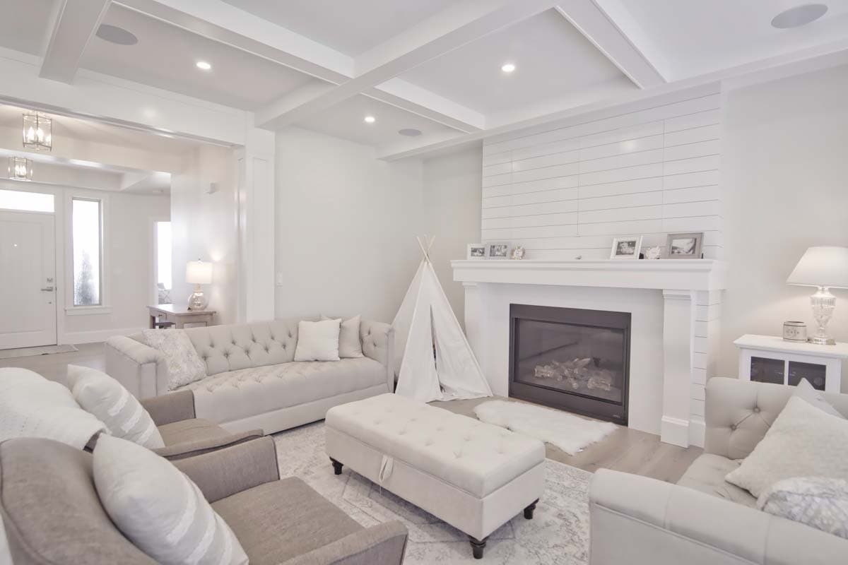 Living room with coffered ceiling, fireplace with shiplap surround, tufted sofas, and storage ottoman.