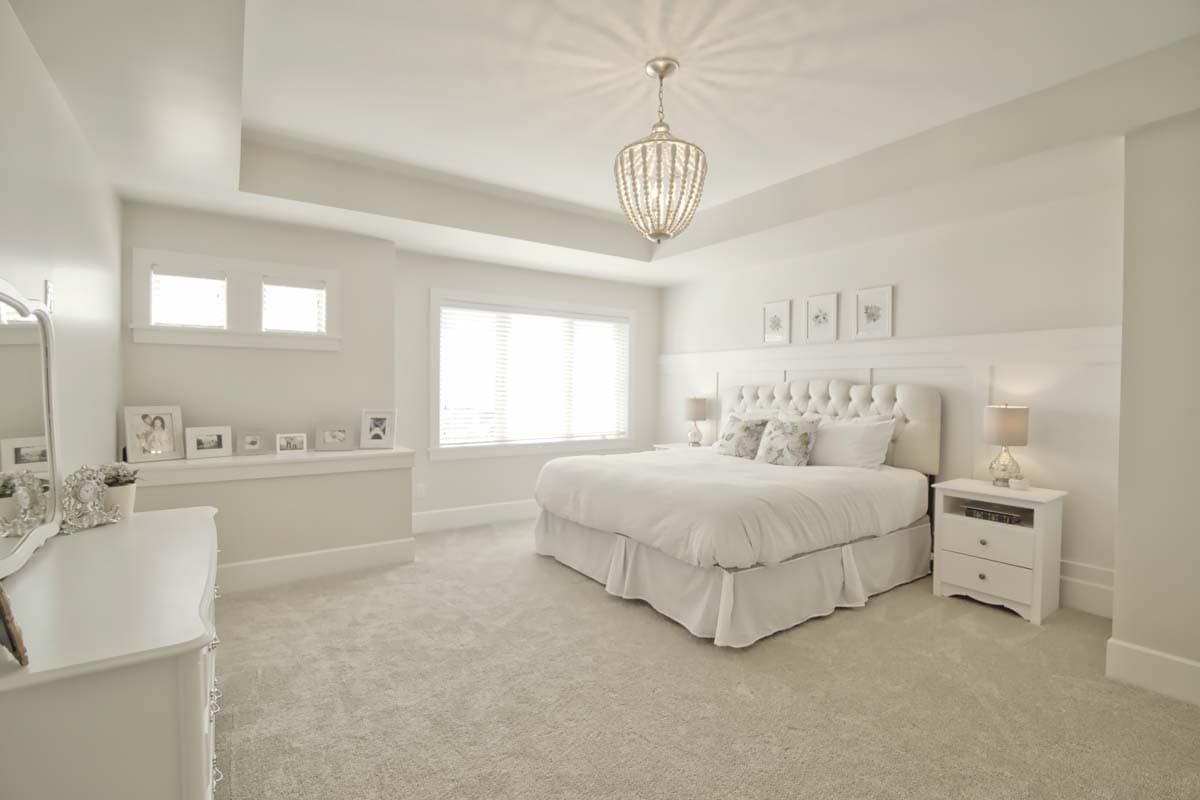 Bedroom with tufted headboard, tray ceiling, large window with blinds, and decorative chandelier.