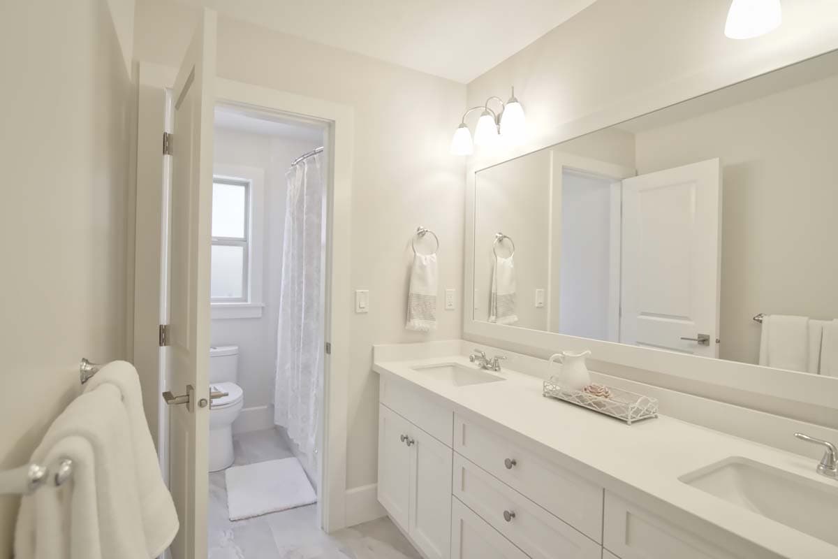 Bathroom with double vanity, large mirror, and adjacent toilet and shower area with window.