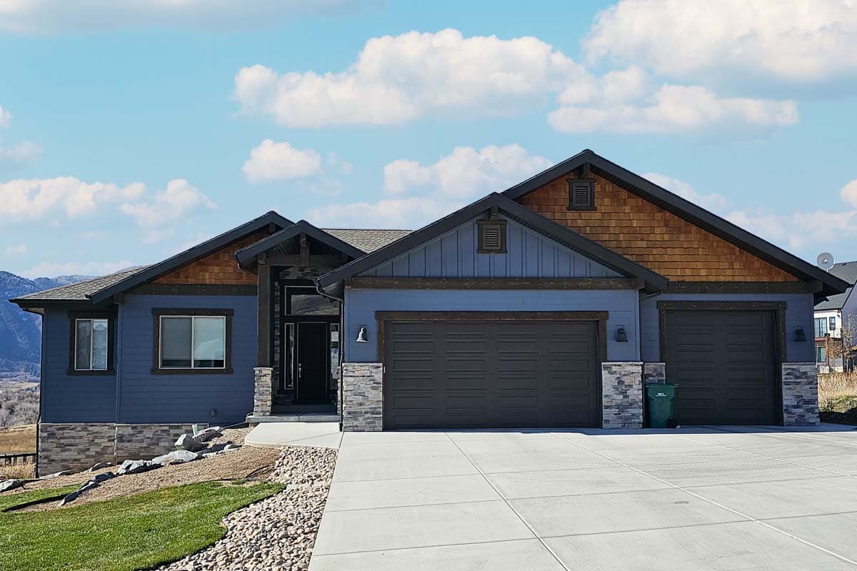 House plan exterior. Ranch style with two stories, gabled roof, stone accents, and two-car garage. Features wood shake roof accents.