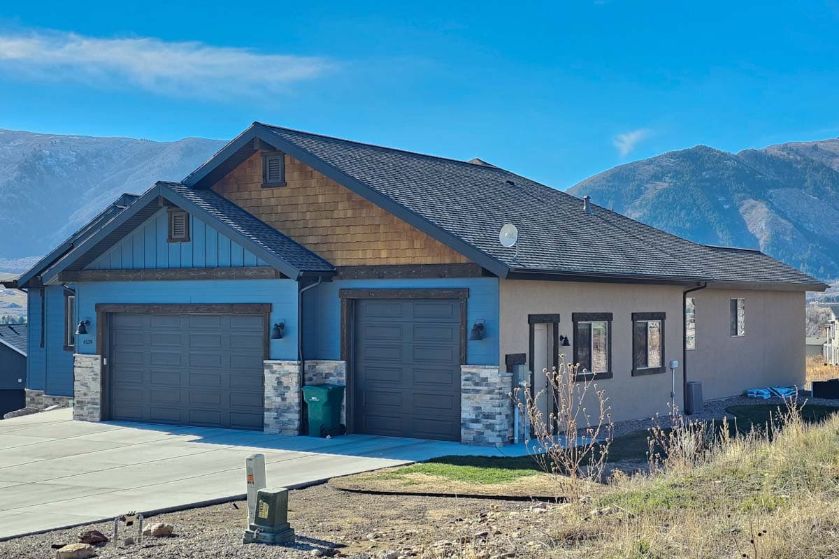 House plan exterior with blue siding, wood shake gables, two-car garage, and stone accents.