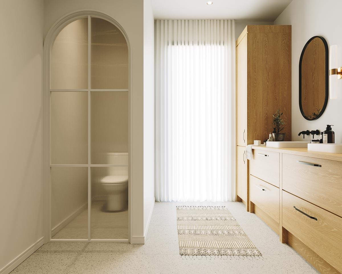 Modern bathroom with a toilet behind a ribbed glass door. Features light wood vanity, a patterned rug, and a large oval mirror.