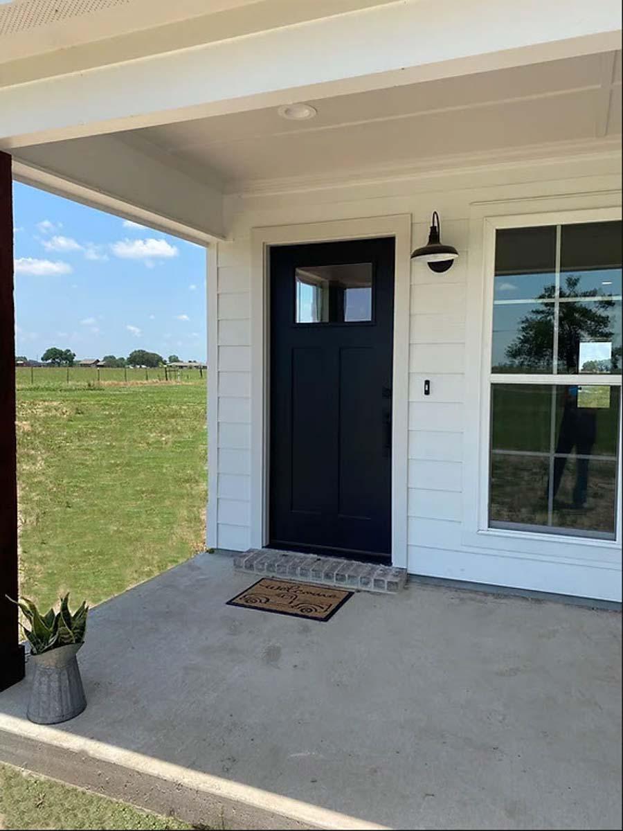 House plan exterior with covered front porch, black paneled door with glass, and white lap siding.