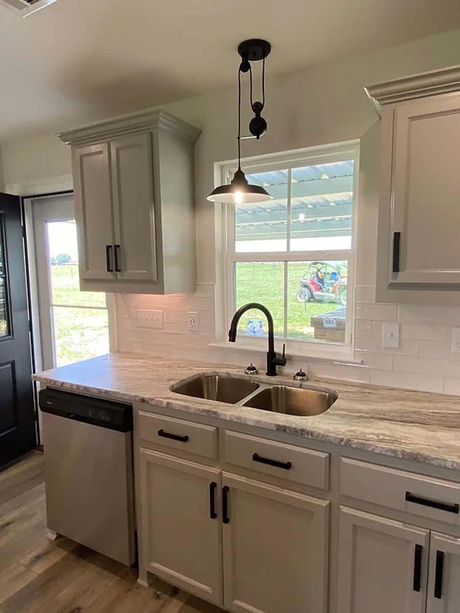 Kitchen with dual-basin sink, black faucet, granite countertops, white subway tile backsplash, and gray Shaker cabinets.