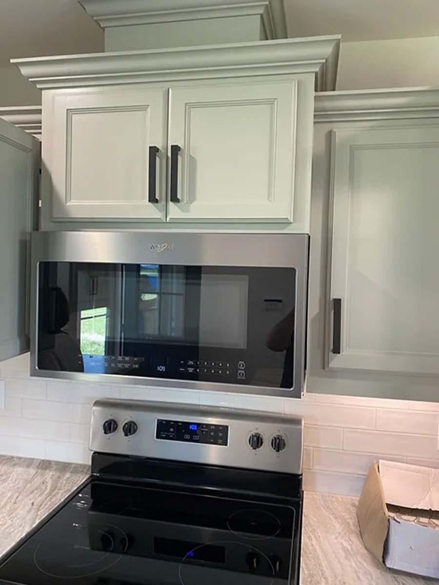 Kitchen area with white subway tile backsplash, stainless steel microwave, and light gray cabinets with black hardware.