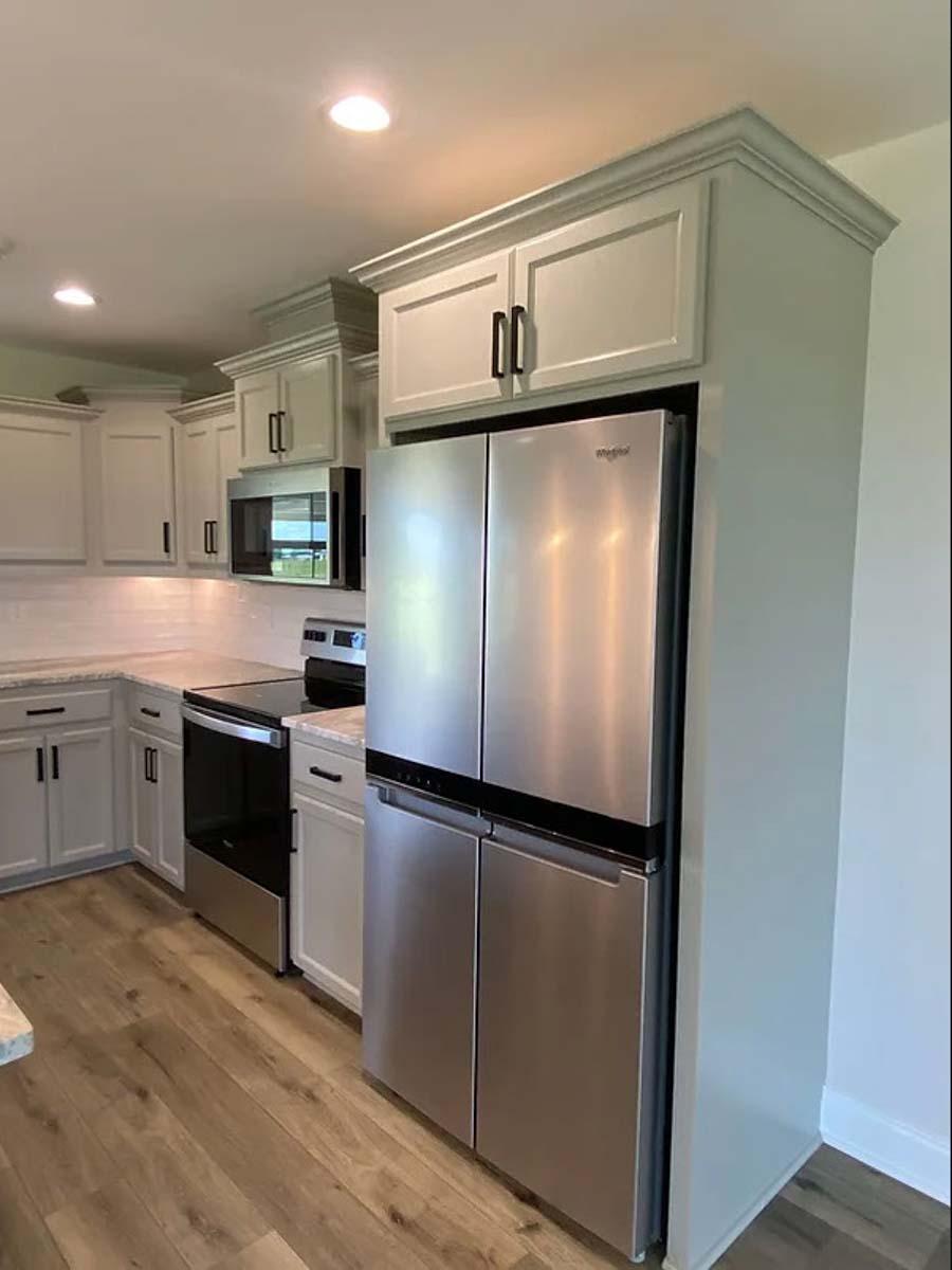 Modern kitchen with stainless steel French door refrigerator, white cabinets, tile backsplash, and wood-look flooring.