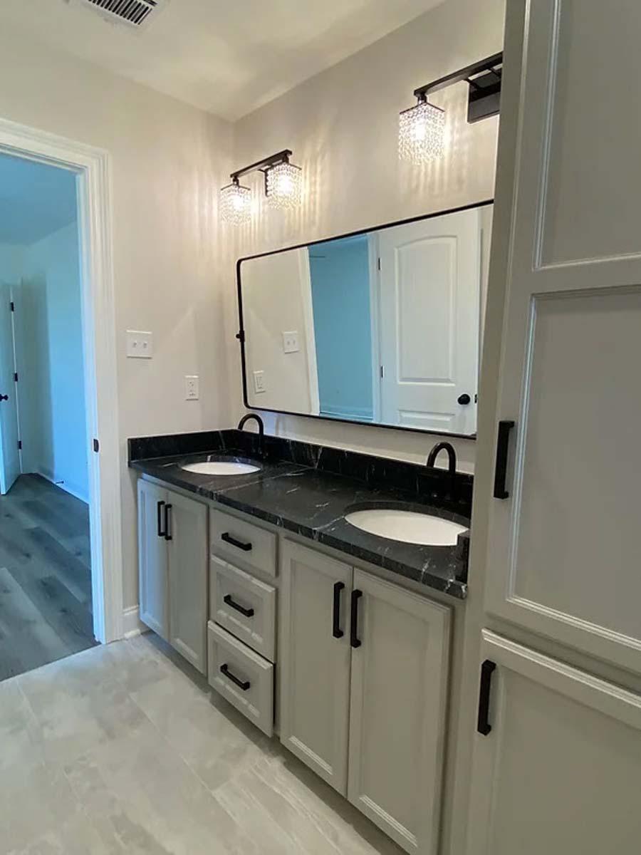 Bathroom vanity with dual sinks, black granite countertop, light gray cabinets, and modern light fixtures.