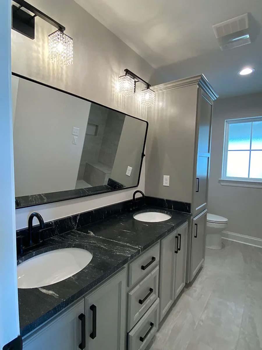 Bathroom vanity with double sinks, black granite countertop, light gray cabinets, and a large mirror with crystal sconces above.