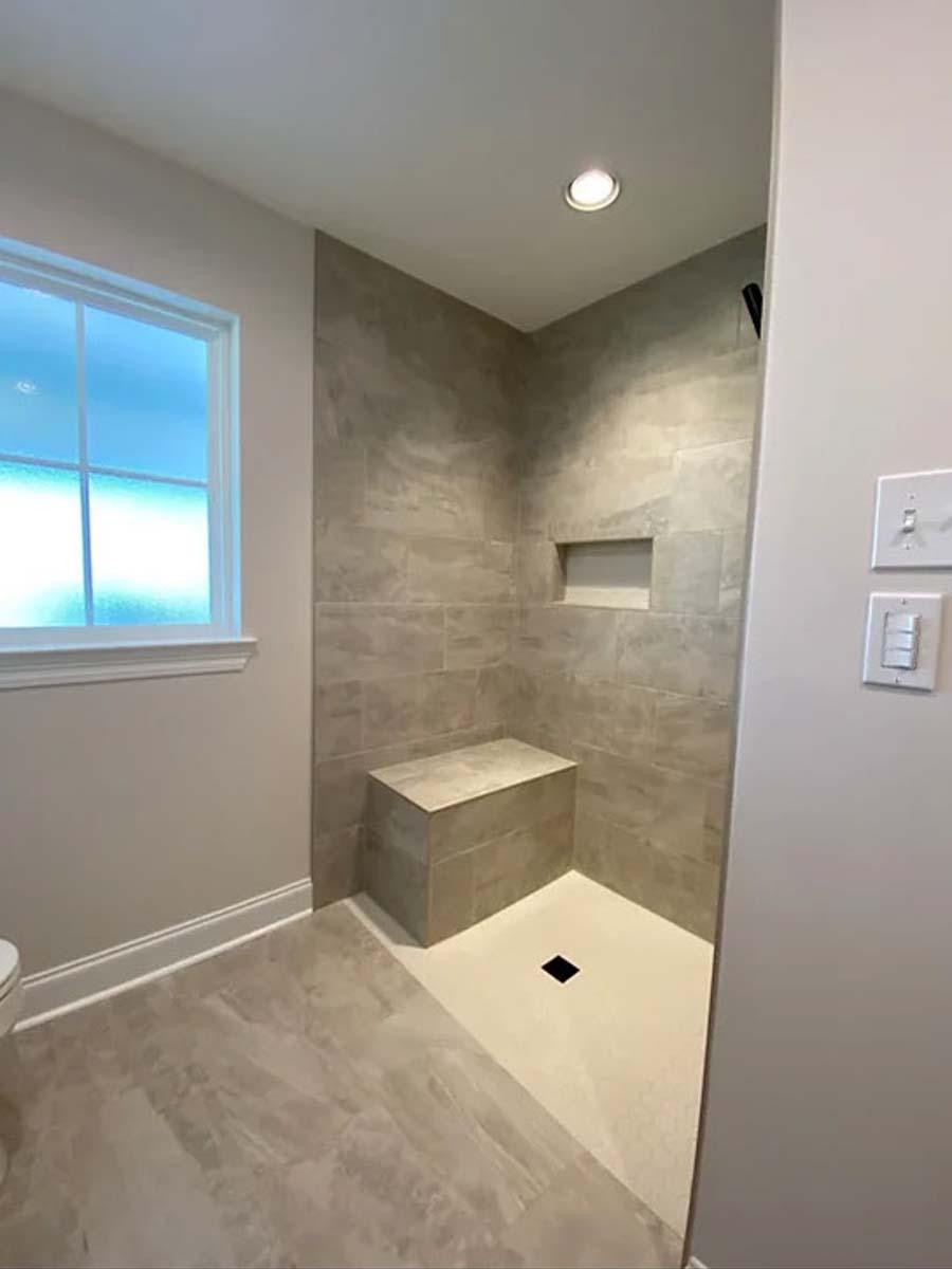 Bathroom featuring a walk-in shower with tile walls, built-in bench, and niche. Marble-look floor and window visible.