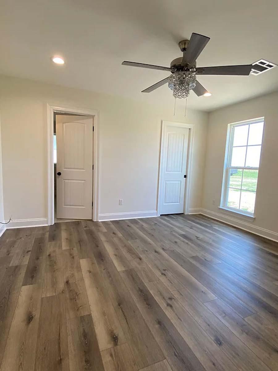 Interior view of a room with wood-look flooring, two doors, a window, and a ceiling fan with a crystal accent.