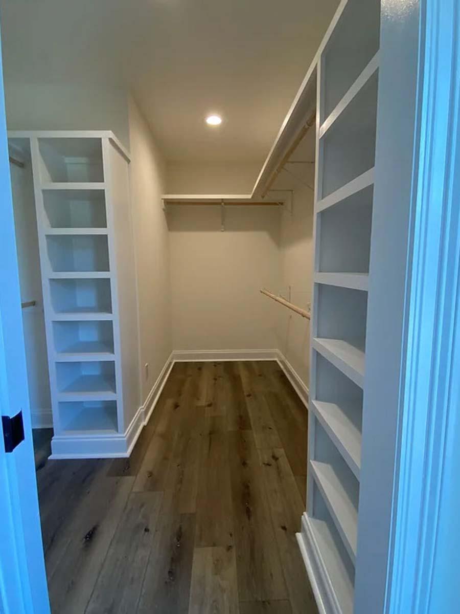 Walk-in closet with built-in shelving on three walls, clothing rods, and wood-look flooring.