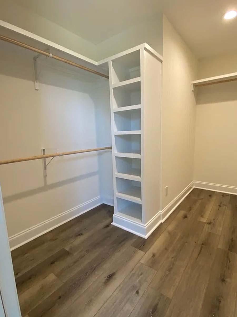 Walk-in closet with built-in shelving unit, two-tiered hanging rods, and wood-look flooring.